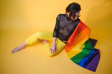 Eşcinsel gurur bayrağı taşıyan eşcinsel adam gülümsüyor ve sarı arka plana bakıyor..