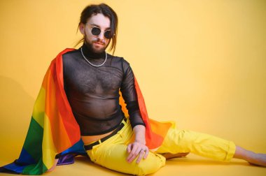 Beyaz arka planda LGBT Rainbow bayrağı taşıyan gururlu, yakışıklı genç bir adam. Eşcinsel gurur bayrağı taşıyan adam