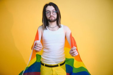 Beyaz arka planda LGBT Rainbow bayrağı taşıyan gururlu, yakışıklı genç bir adam. Eşcinsel gurur bayrağı taşıyan adam