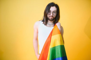 Beyaz arka planda LGBT Rainbow bayrağı taşıyan gururlu, yakışıklı genç bir adam. Eşcinsel gurur bayrağı taşıyan adam
