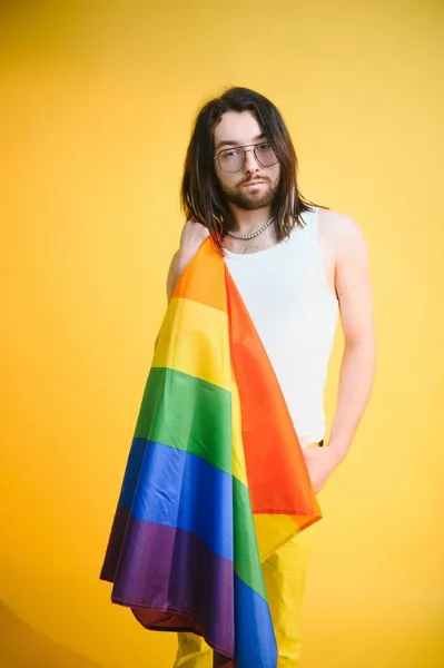 Handsome young man with pride movement LGBT Rainbow flag on shoulder against white background. Man with a gay pride flag