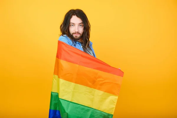 gay man with a gay pride flag smiling and looking away on yellow background