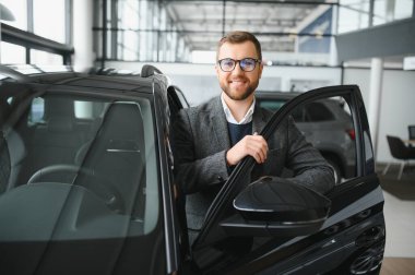 Araba galerisini ziyaret ediyorum. Yakışıklı sakallı adam yeni arabasını okşuyor ve gülümsüyor..