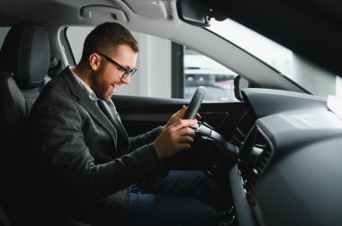 Araba galerisini ziyaret ediyorum. Yakışıklı sakallı adam yeni arabasını okşuyor ve gülümsüyor..