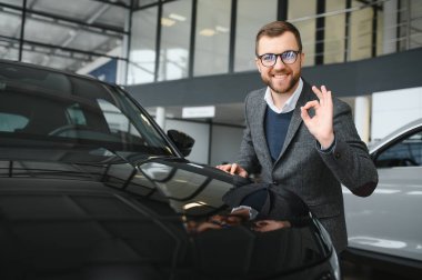 Araba galerisini ziyaret ediyorum. Yakışıklı sakallı adam yeni arabasını okşuyor ve gülümsüyor..