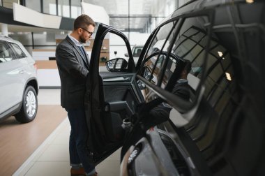 Araba galerisini ziyaret ediyorum. Yakışıklı sakallı adam yeni arabasını okşuyor ve gülümsüyor..