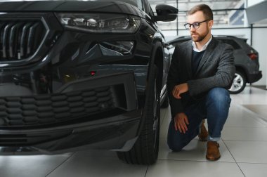 Araba galerisini ziyaret ediyorum. Yakışıklı sakallı adam yeni arabasını okşuyor ve gülümsüyor..