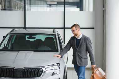 Araba galerisini ziyaret ediyorum. Yakışıklı sakallı adam yeni arabasını okşuyor ve gülümsüyor..