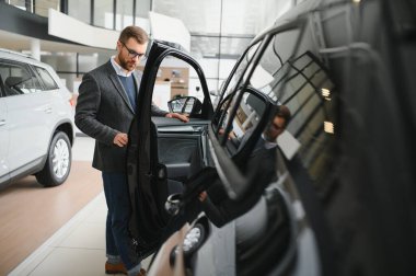 Adam akıllı müşteri, takım elbiseli müşteri, otomobili seçer, kenara bakar, galeride yeni otomobil almak ister.