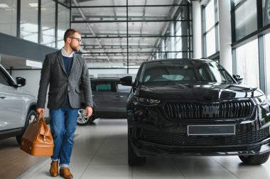 Seçimini yapıyor. Takım elbiseli bir gencin yatay portresi. Arabaya bakıyor ve satın almalı mı diye düşünüyor..