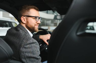 Araba galerisini ziyaret ediyorum. Yakışıklı sakallı adam yeni arabasını okşuyor ve gülümsüyor..