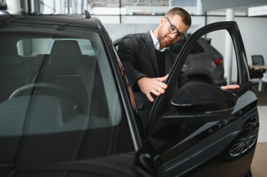 Araba galerisini ziyaret ediyorum. Yakışıklı sakallı adam yeni arabasını okşuyor ve gülümsüyor..