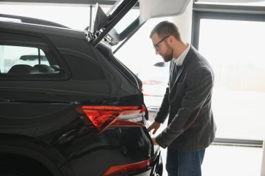 Araba galerisini ziyaret ediyorum. Yakışıklı sakallı adam yeni arabasını okşuyor ve gülümsüyor..