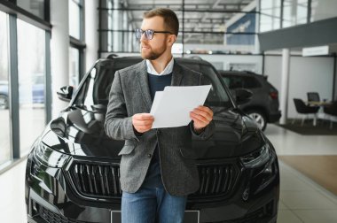 İyi görünümlü, neşeli ve samimi satıcı bir araba salonu veya showroom pozlar