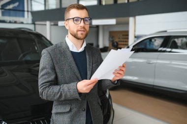 İyi görünümlü, neşeli ve samimi satıcı bir araba salonu veya showroom pozlar