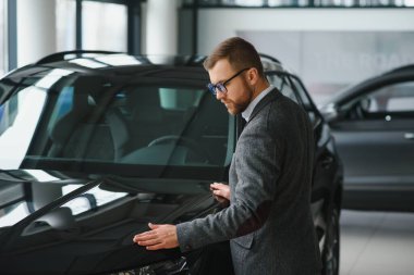 Araba galerisini ziyaret ediyorum. Yakışıklı sakallı adam yeni arabasını okşuyor ve gülümsüyor..