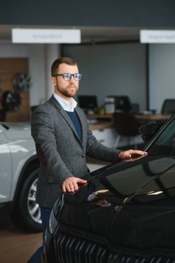 Adam akıllı müşteri, takım elbiseli müşteri, otomobili seçer, kenara bakar, galeride yeni otomobil almak ister.