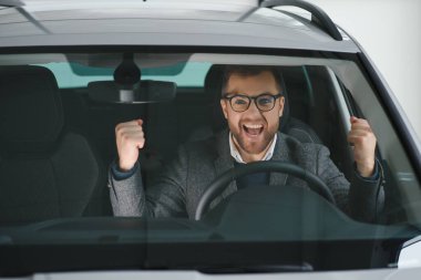 Araba galerisini ziyaret ediyorum. Yakışıklı sakallı adam yeni arabasını okşuyor ve gülümsüyor..