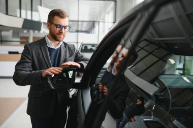 Araba galerisini ziyaret ediyorum. Yakışıklı sakallı adam yeni arabasını okşuyor ve gülümsüyor..