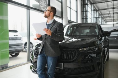 İyi görünümlü, neşeli ve samimi satıcı bir araba salonu veya showroom pozlar