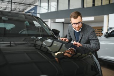 Araba galerisini ziyaret ediyorum. Yakışıklı sakallı adam yeni arabasını okşuyor ve gülümsüyor..