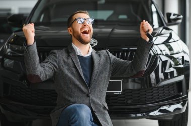 Yeni bir arabanın mutlu sahibi. Günlük giysiler içinde duygusal açıdan yakışıklı bir adam, galeriden bir araba almaktan mutlu.