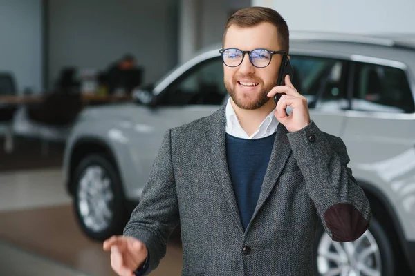 stock image Good looking, cheerful and friendly salesman poses in a car salon or showroom