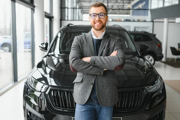 stock image Good looking, cheerful and friendly salesman poses in a car salon or showroom