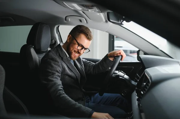 Handsome businessman driving car to airport, going on business side view, copy space. Happy man in stylish suit going to business meeting in the morning, driving his luxury car, shot from cabin