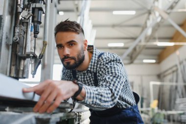 Endüstriyel fabrikada çalışan erkek fabrika işçisi, güvenlik üniforması ve başlık giyerken makineyle birlikte çalışıyor.