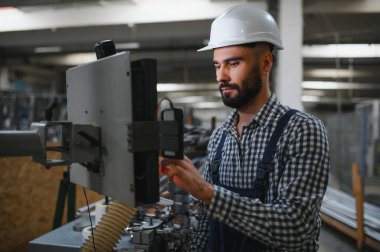 Profesyonel Ağır Sanayi Mühendisi, Güvenlik Üniforması Giyen İşçi, Sert Şapka Gülümseyen. Arka planda Odaklanmamış Büyük Endüstriyel Fabrika