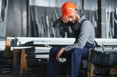 Profesyonel Ağır Sanayi Mühendisi, Güvenlik Üniforması Giyen İşçi, Sert Şapka Gülümseyen. Arka planda Odaklanmamış Büyük Endüstriyel Fabrika