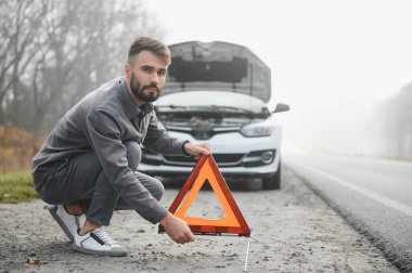 Sad man near broken car searching help in field.