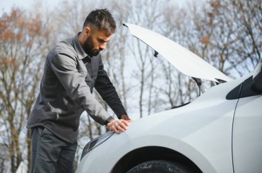 Kırık bir araba ile yol kenarında açık bir kaputa yakınındaki genç bir adam