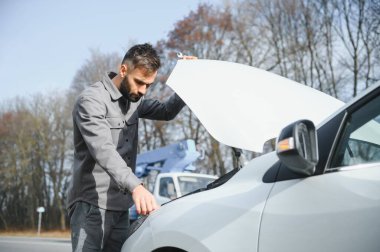 Kırık bir araba ile yol kenarında açık bir kaputa yakınındaki genç bir adam