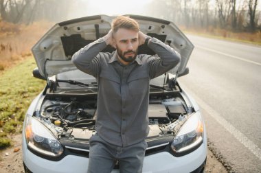Yolda bozuk bir arabanın yanında duran üzgün şoför kafasını tutuyor. Araba arızası kavramı.