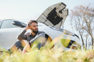 Yolda bozuk bir arabanın yanında duran üzgün şoför kafasını tutuyor. Araba arızası kavramı.