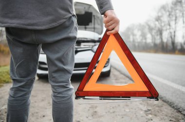 Kırık bir araba ile yol kenarında açık bir kaputa yakınındaki genç bir adam