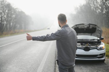 Sad man near broken car searching help in field.