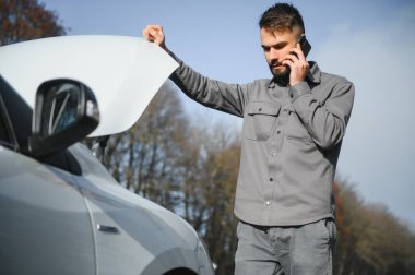 Kırık bir araba ile yol kenarında açık bir kaputa yakınındaki genç bir adam