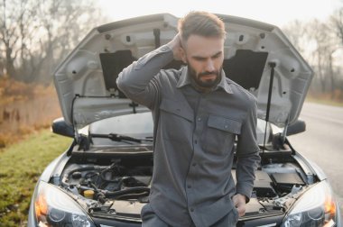 Sad driver calling car service, opening hood, having engine problem standing near broken car on the road. Car breakdown concept.