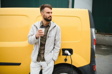 Yakışıklı adam elektrikli araba şarj ederken kahve içme.