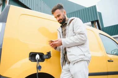 Elektrikli arabanın yanında şarj işleminin bitmesini bekleyen sıradan bir adam..