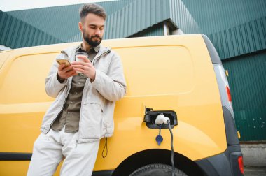 Küçük bir kamu istasyonundan şarj olan genç ve mutlu bir adam.