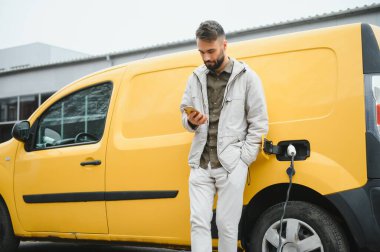 Elektrikli arabanın yanında şarj işleminin bitmesini bekleyen sıradan bir adam..