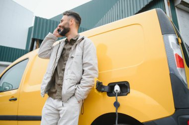 Elektrikli arabanın yanında şarj işleminin bitmesini bekleyen sıradan bir adam..