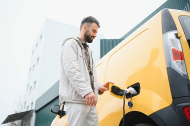 Elektrikli arabanın yanında şarj işleminin bitmesini bekleyen sıradan bir adam..