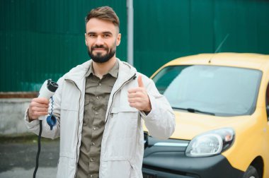 Şarj kablosunun yanında duran genç bir adamın portresi..