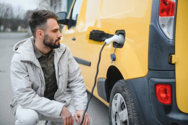 Küçük bir kamu istasyonundan şarj olan genç ve mutlu bir adam.