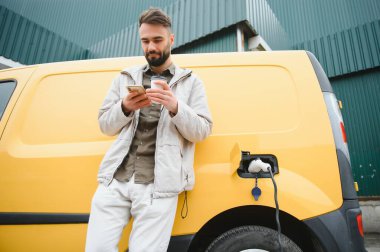 Elektrikli arabanın yanında şarj işleminin bitmesini bekleyen sıradan bir adam..